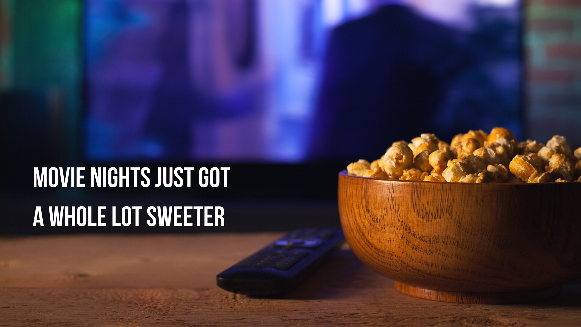Wooden bowl of popcorn on a table with a blurred TV in the background, text 'MOVIE NIGHTS JUST GOT A WHOLE LOT SWEETER'.